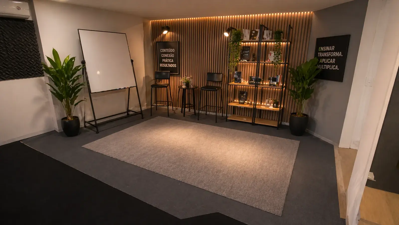 Auditório do Hub vazio com palco, TV cenográfica, painéis acústicos e iluminação warm